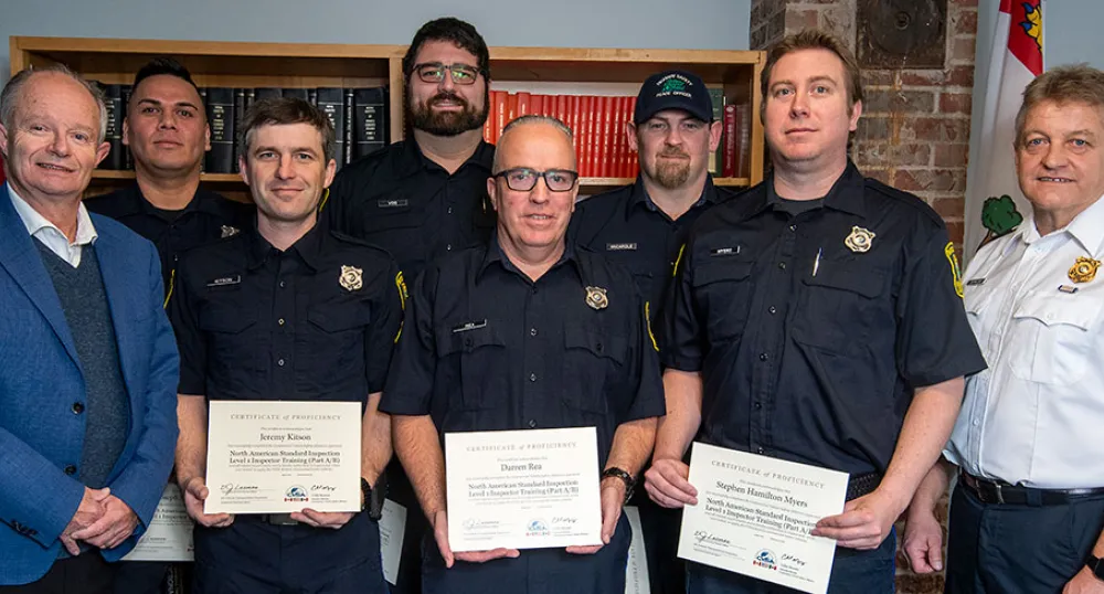 image of a group of people in a room, standing shoulder to shoulder with some holding certificates and book cases in the background
