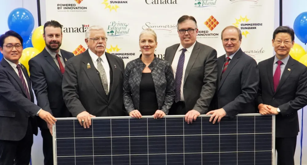 People standing shoulder to shoulder behind a solar panel.