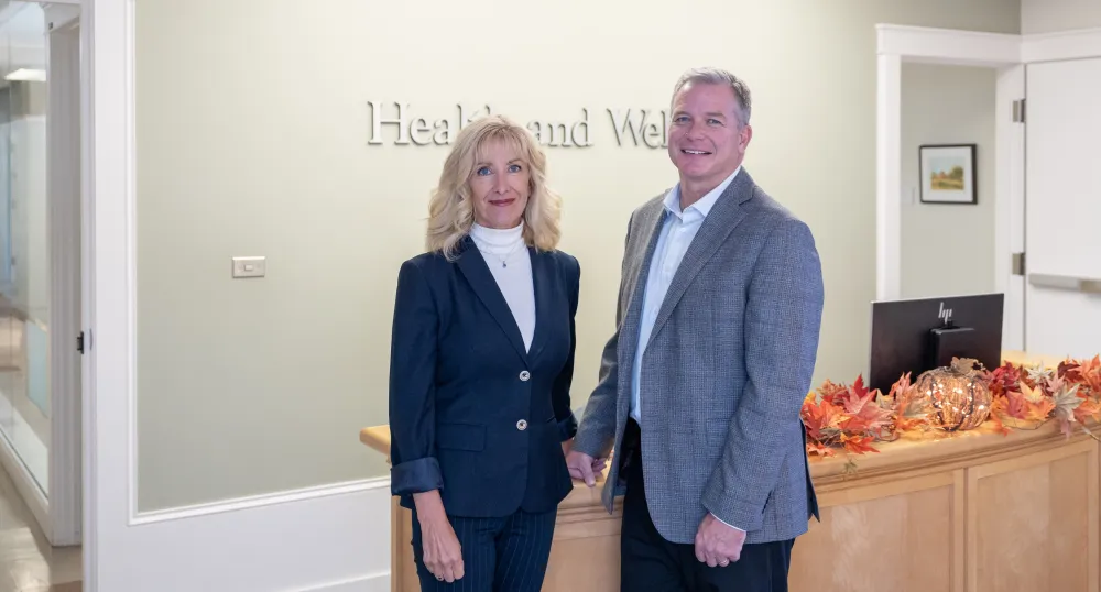 image of two people standing side by side in front of a desk in an office foyer