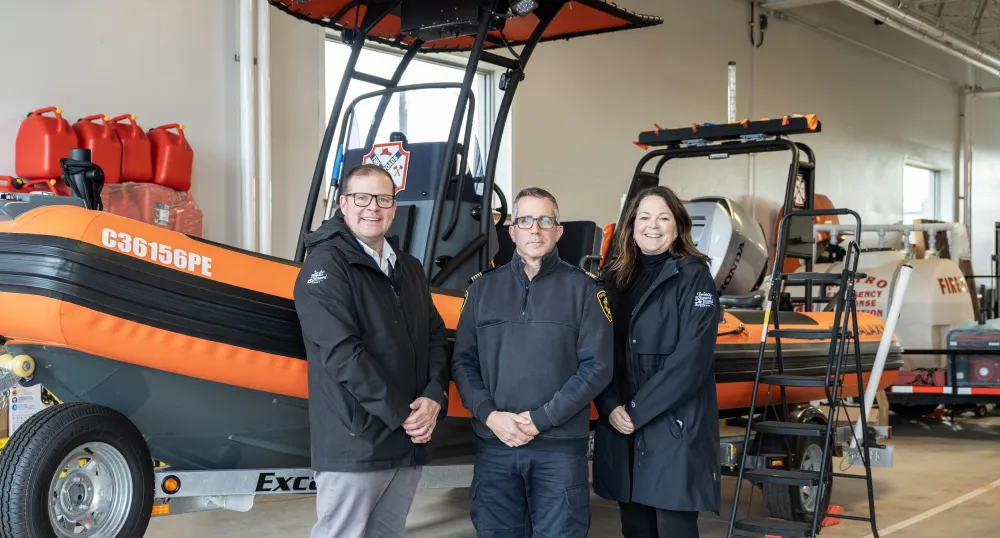 image de trois personnes devant un petit bateau de sauvetage dans un garage