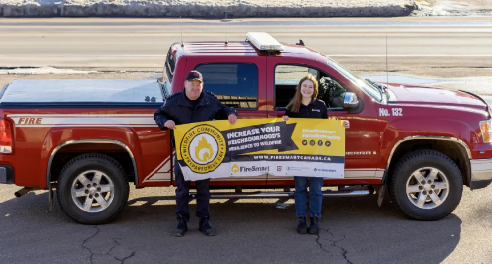 A man and woman stand outside in front of a fire truck holding a sign advertising the Fire Smart program
