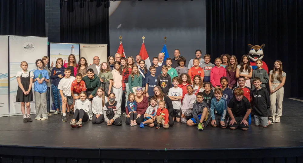 image of a large group of young students and some adults on a performance stage with flags in the background