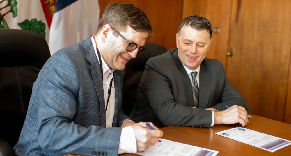 Two people sitting shoulder to shoulder at a desk signing a document.