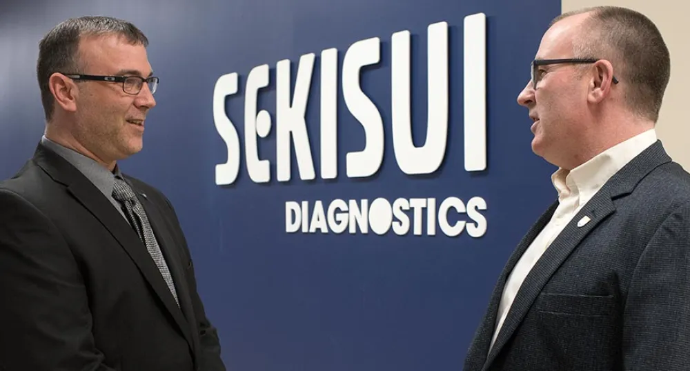 Two people standing in front of a sign at Sekisui Diagnostics