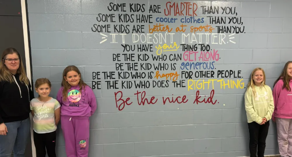 image of a teacher and elementary students standing near a wall with some inspirational writing on it.