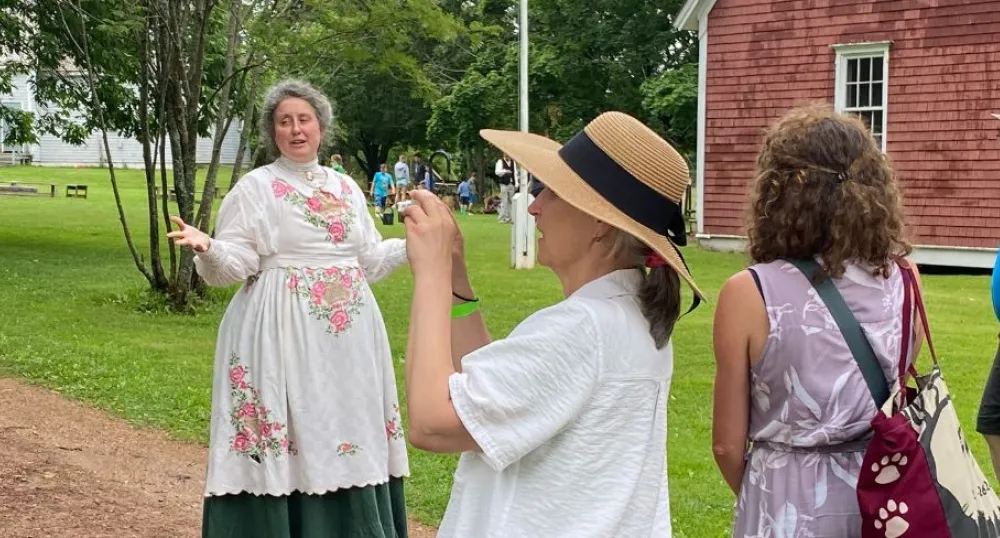 image of a person in 1800s clothing speaking to some people outside a barn
