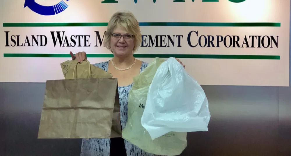 Merie Surkan stands in front of the IWMC sign holding paper and plastic bags