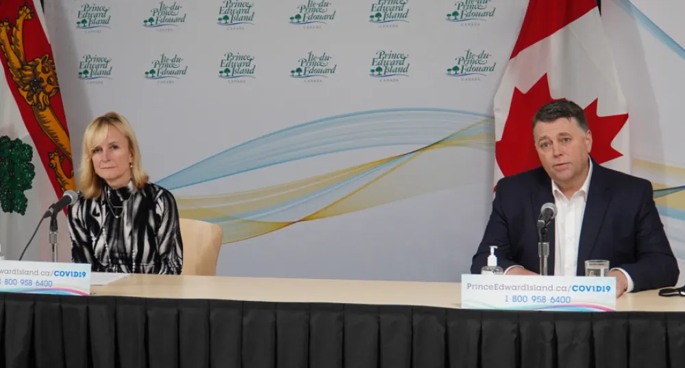 image of two people sitting behind a long table with flags behind them.