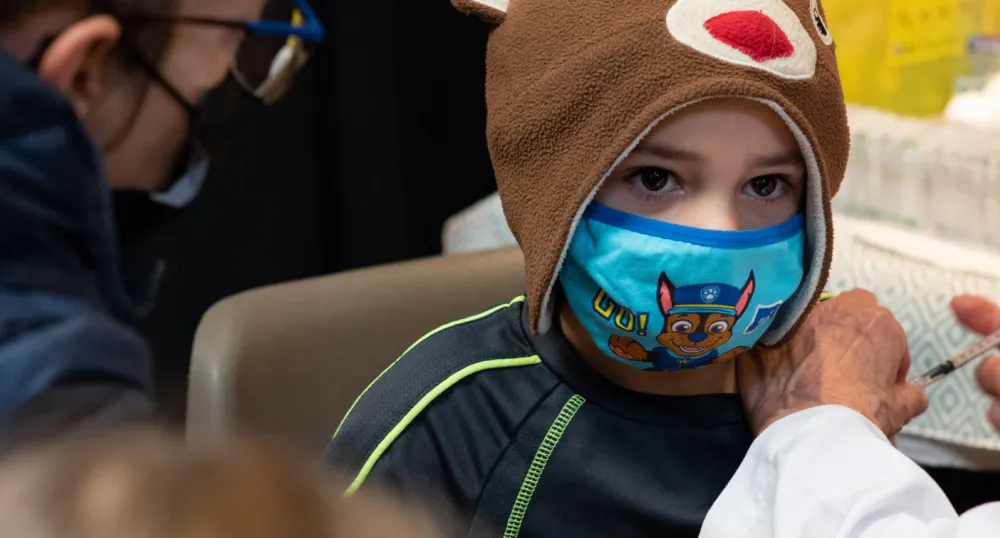 image of a child with a mask on receiving his vaccination