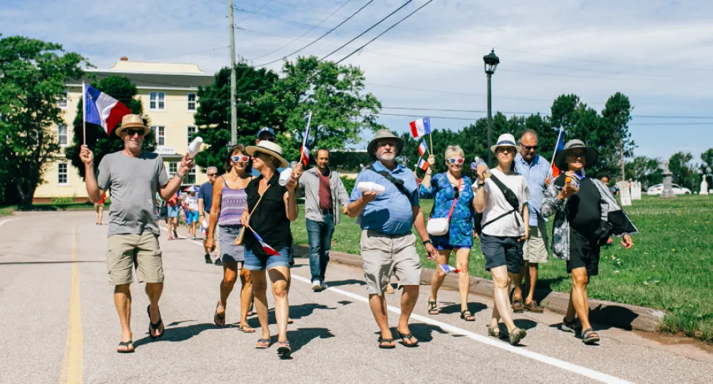 image of people marching on a small country street during summertime and each are holding small flags
