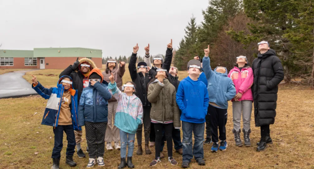 image of a small group of elementary students wearing lunar eclipse glasses looking skyward and pointing.