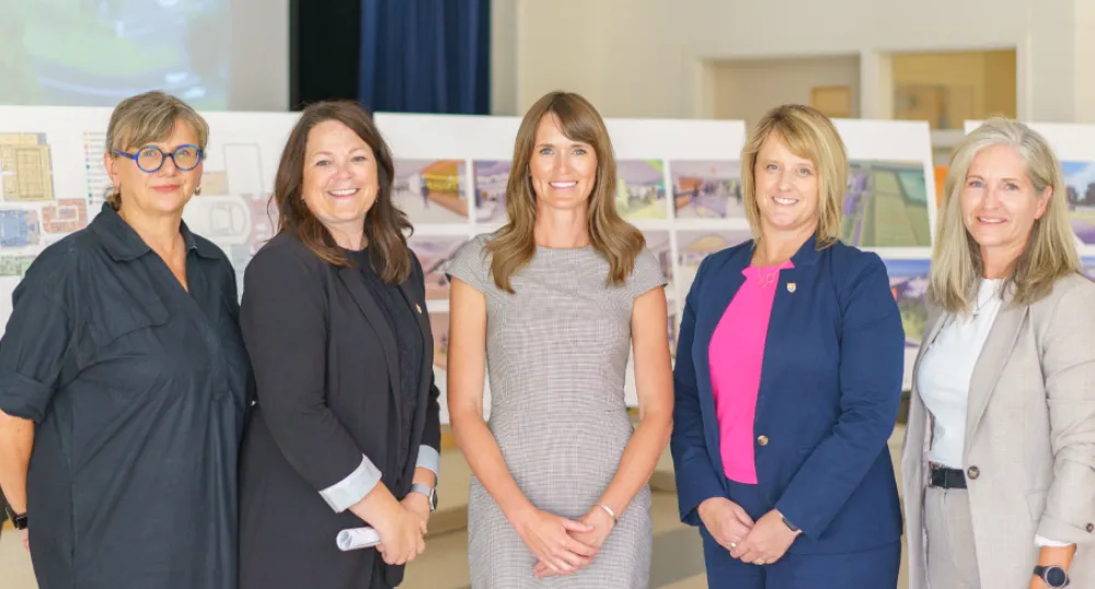 image of five people standing shoulder to shoulder in front of some architectural drawings of a  high school
