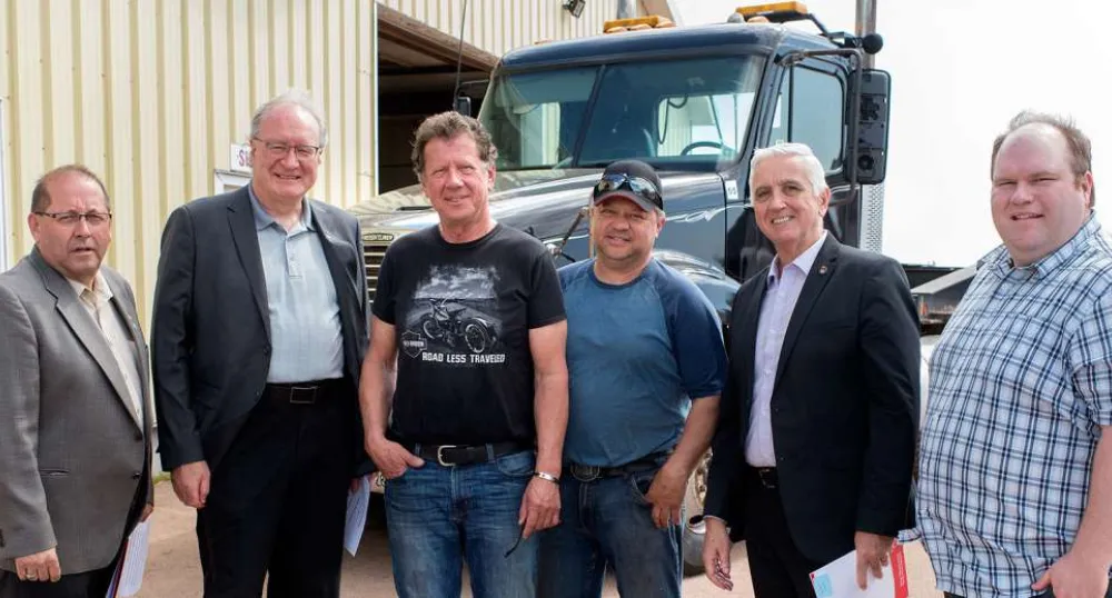 Six people standing with a large truck in the background.
