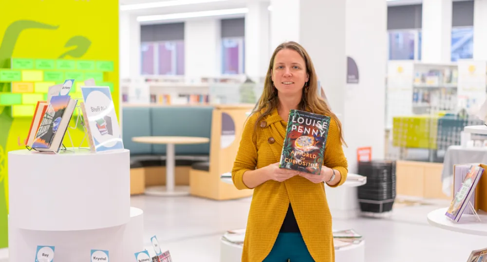 image of a person standing in a library holding a book in front of her