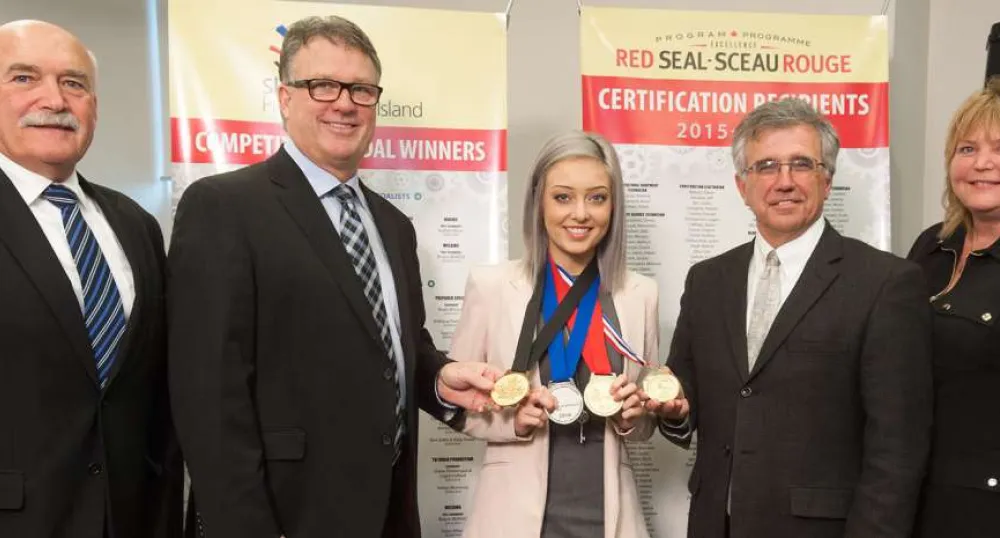 People standing in front of pop-up banners with middle person displaying medals won at a national competition.