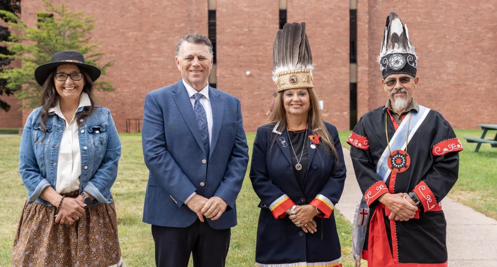 image of four people standing shoulder to shoulder with a brick building in the background