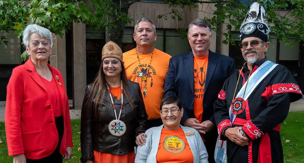 image of a group of people some in colourful ceremonial clothing standing shoulder to shoulder in front of a building