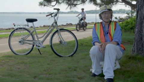 image of a person wearing a cycling helmet sitting beside a tree and a bicycle