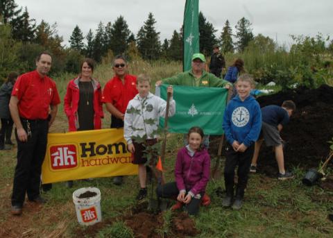 Students and adults stand with shovels and dirt, ready for tree planting.