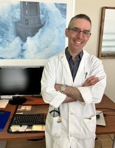 A smiling man wearing the white coat of a family physician