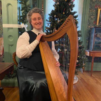 image d'une personne vêtue de vêtements des années 1800 jouant de la harpe dans une salle d'époque décorée pour Noël