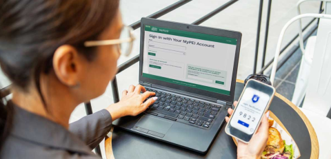 Person using a laptop with a MyPEI Account login page and holding a smartphone showing a two-factor authentication code.