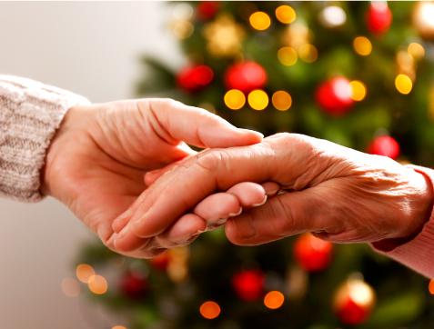 Close-up of two hands gently holding one another in front of a blurred, decorated Christmas tree.
