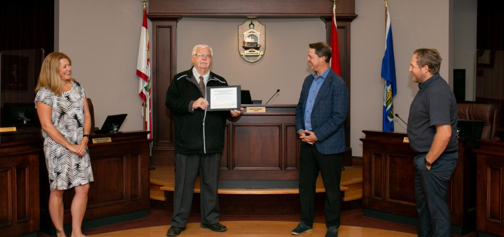 Four officials stand in the Summerside City Hall, with the Mayor holding a certificate. 
