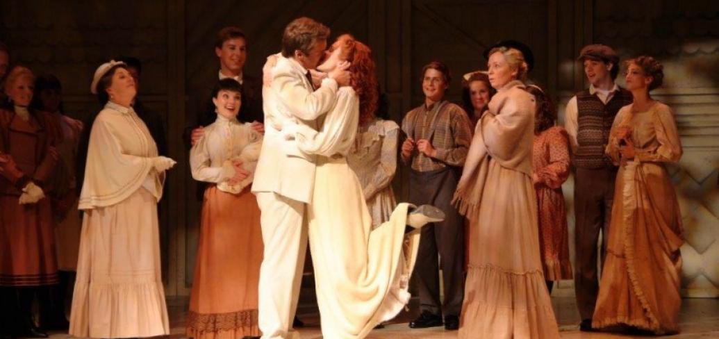 In a scene from Anne & Gilbert the Musical, Anne and Gilbert share a kiss while the towns people look on.