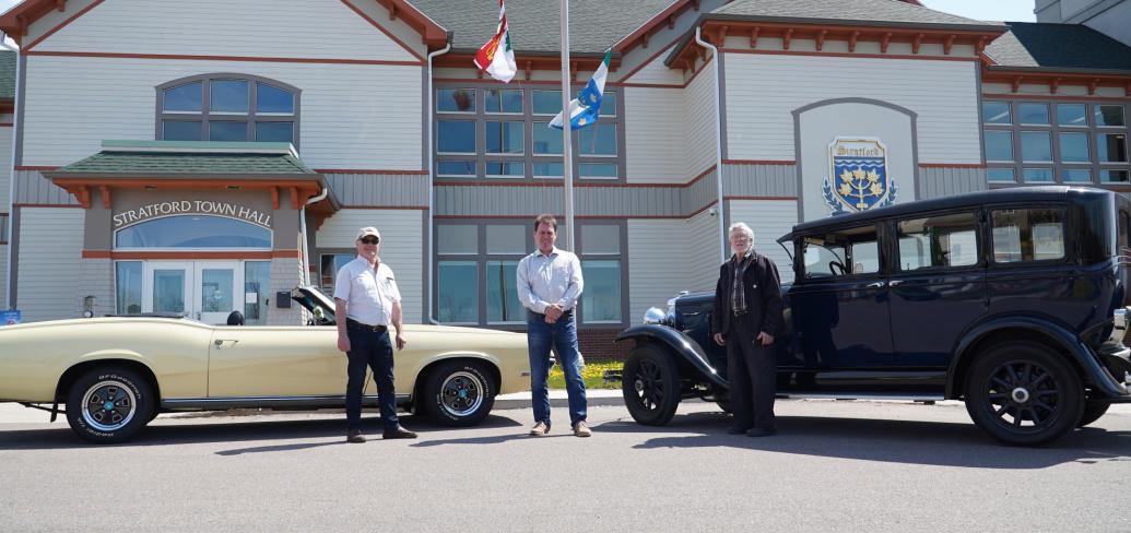 Image of three people standing in front of two antique cars