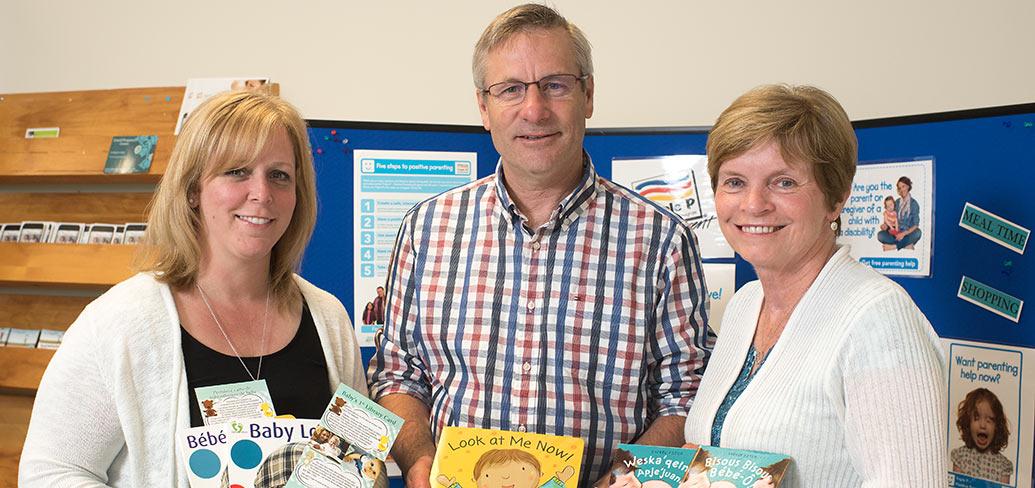 Three people standing together displaying baby books