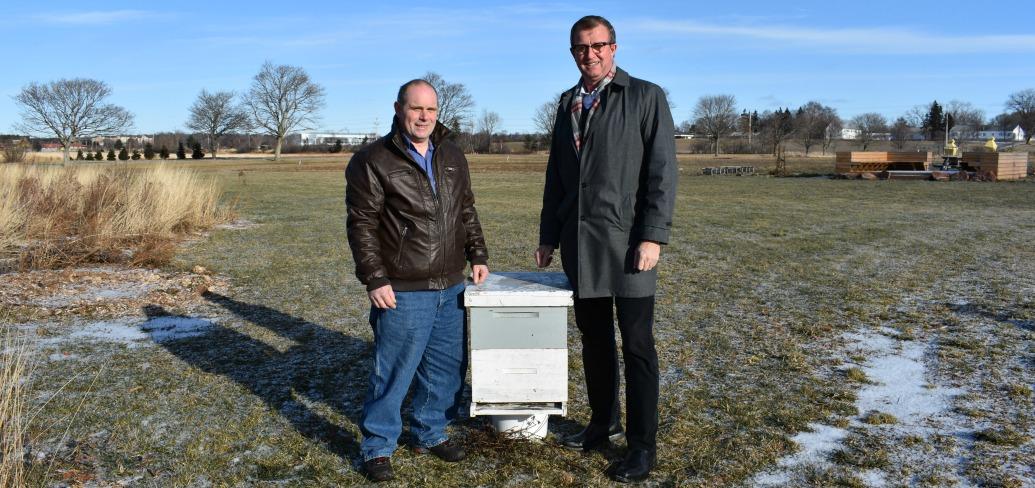 Photo shows two men standing on either side of a box-shaped beehive.