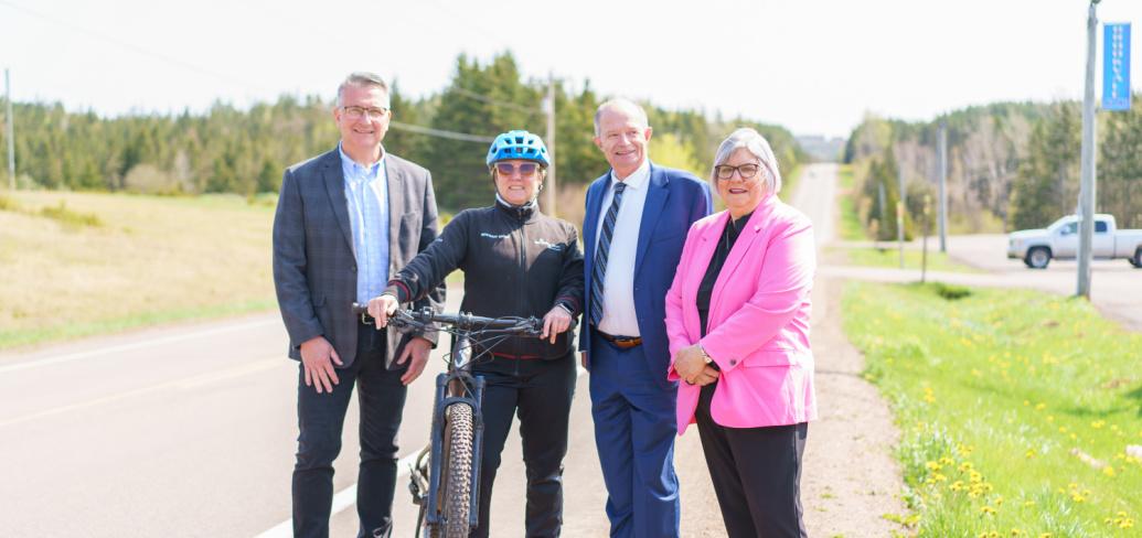 image of four peole standing shoulder to shoulder beside a road and one person holding onto a bicycle