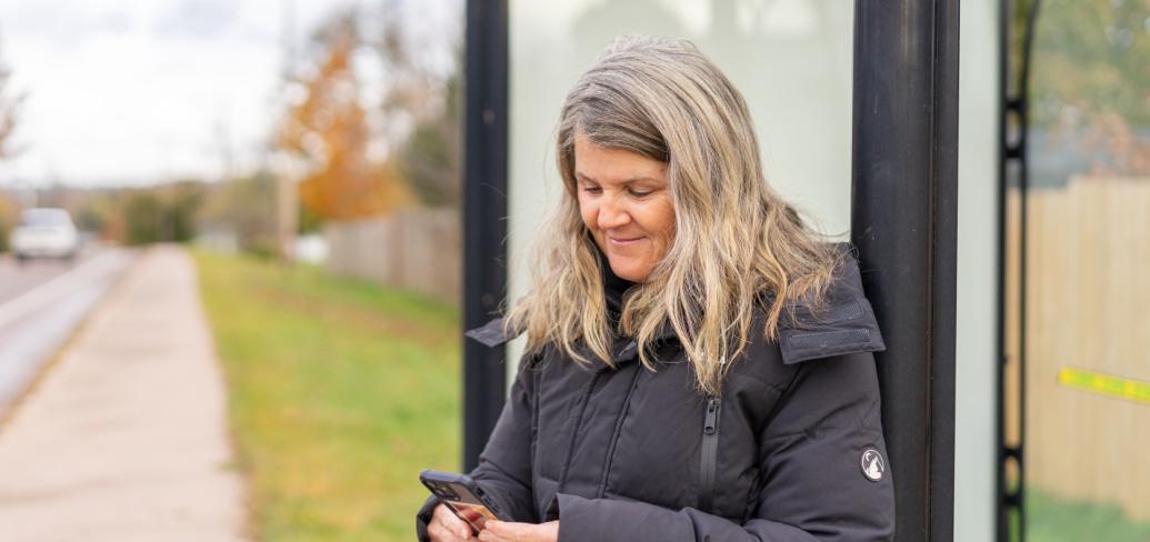 image of a person at a bus stop looking at her cell phone