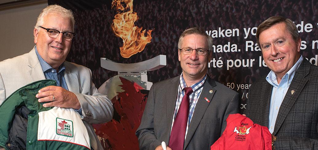Brian McFeely holds a 1991 Canada Games jacket, Health and Wellness Minister Robert Henderson and Wayne Carew hold a 2009 Canada Games jacket at announcement