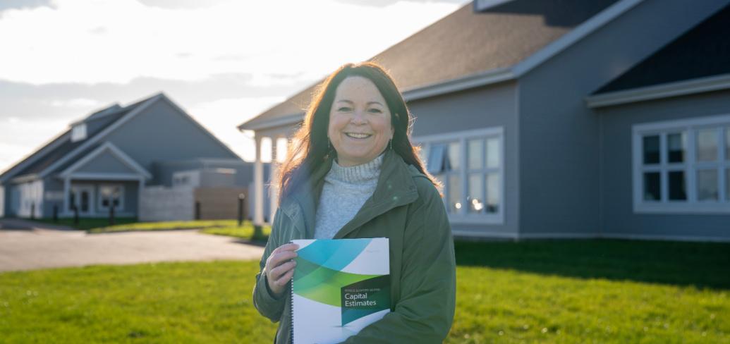 image of a person holding a booklet in front of her with a home in the background