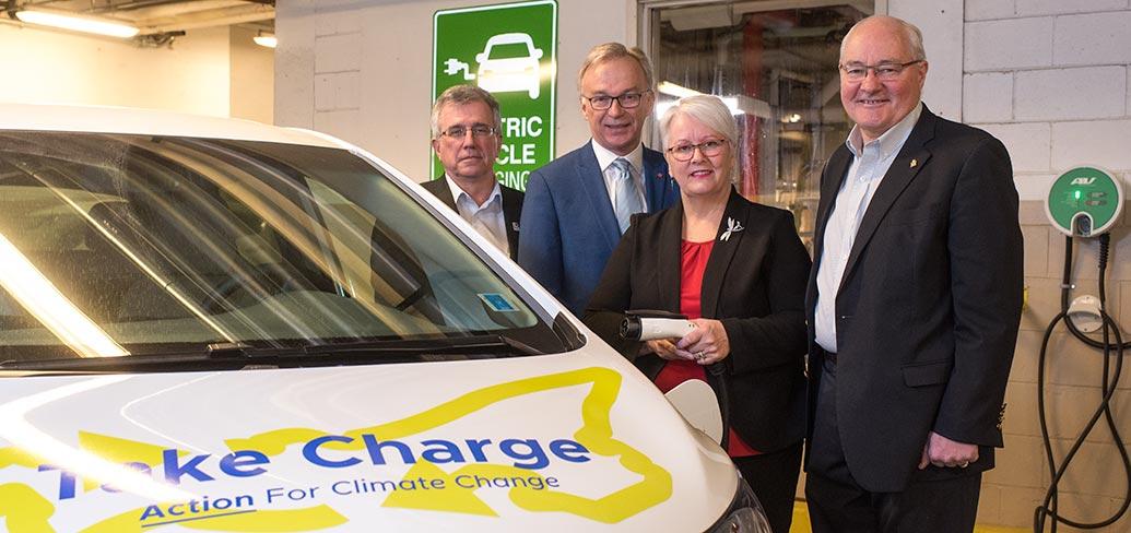 Richard Brown, Sean Casey, Paula Biggar and Wayne Easter stand beside an electric car in front of a charging station