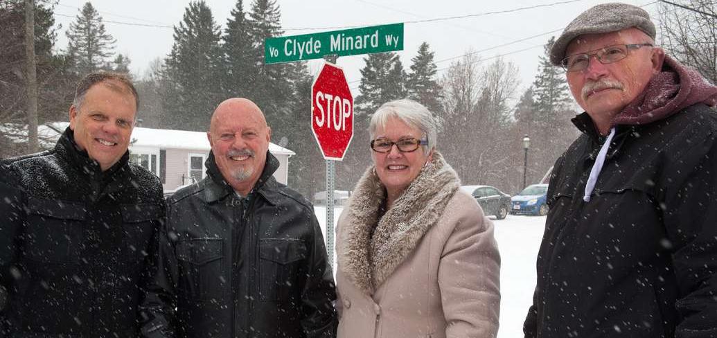Minister Biggar and thre other people stand in front of the Clyde Minard Way street sign.