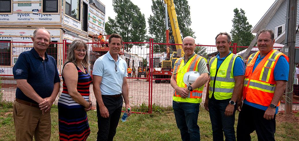 image of six people standing in front of a construction area fence with workers in the background