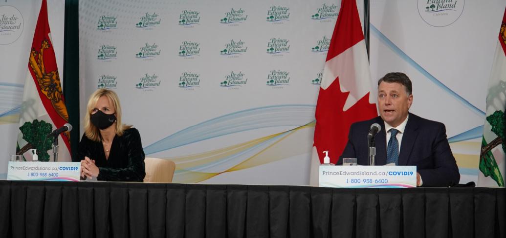 image of two people wearing masks while sitting at a news conference table