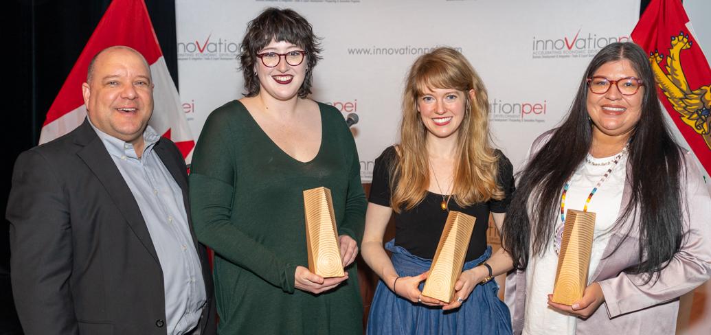 image of  four people standing shoulder to shoulder and some holding onto awards