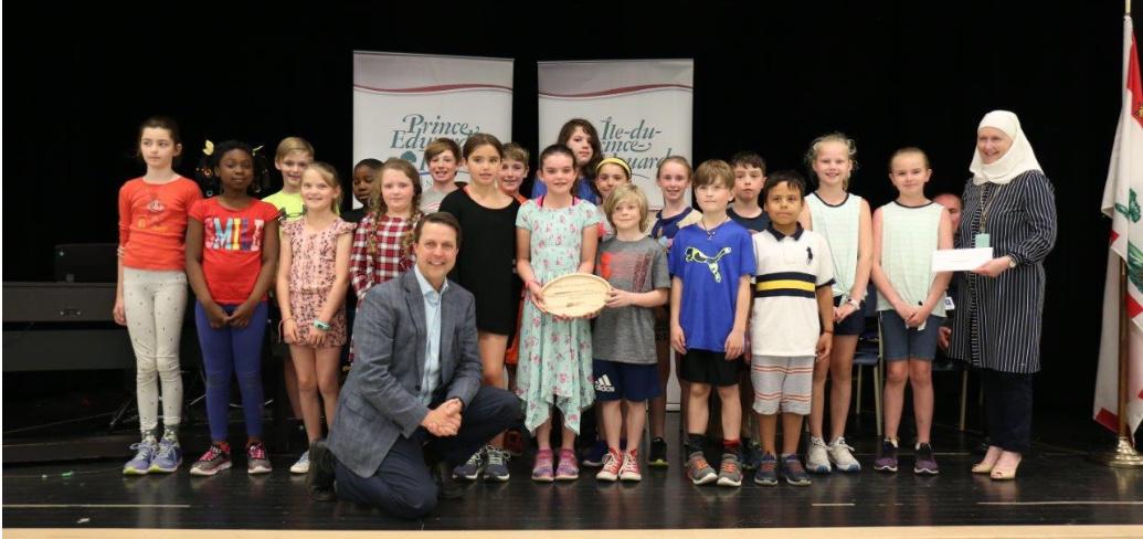 Minister Brad Trivers kneels in front of a group of children from Spring Park School's Grade 4C French Immersion class 