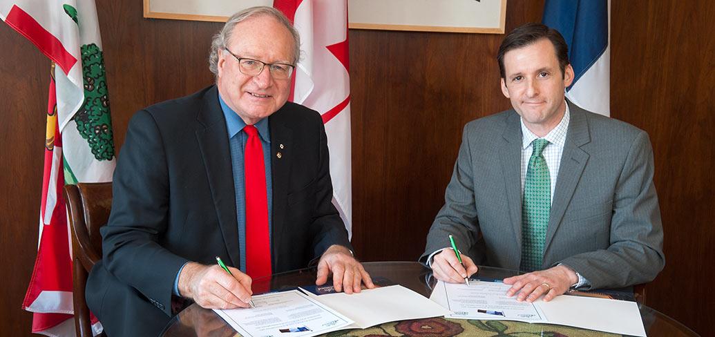 Premier MacLauchlan and Jese Francis sitting at a desk signing documents.