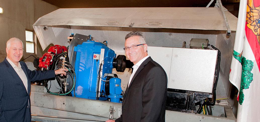 Minister MacDonald and Carl Brothers stand in front of wind trubine machinery under production.