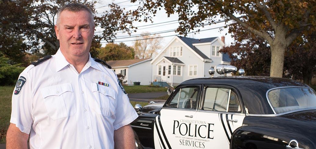 Photo shows Gary McGuigan standing next to Charlottetown Police Services' classic patrol car.