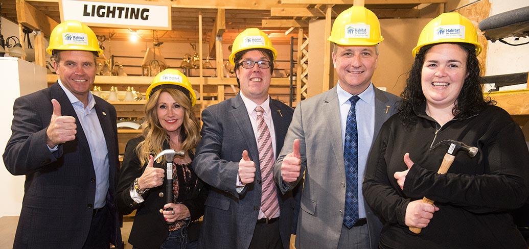 Five people standing side by side wearing hard hats and holding their thumbs up