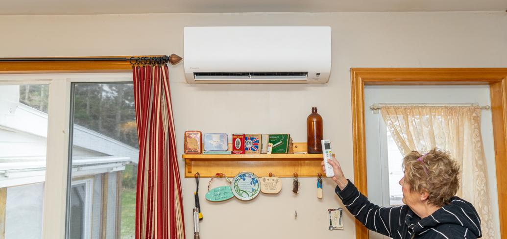 image of a person inside a house using a remote control to use a heat pump