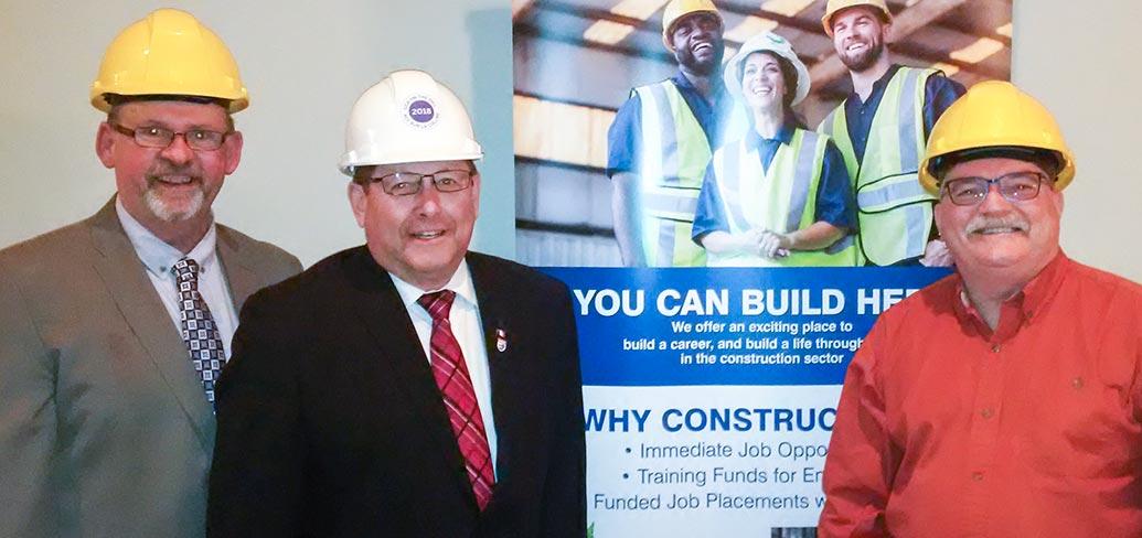Three people standing beside each other wearing hard hats and a banner sign is behind them
