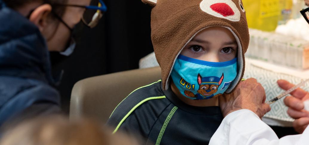 image of a child with a mask on receiving his vaccination
