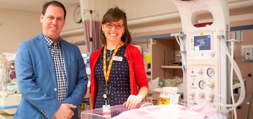 Two people standing beside some infant equipment in a hospital.